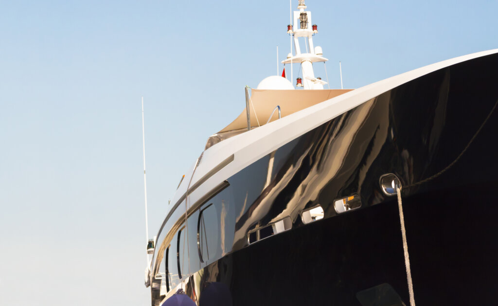Side view of luxury black yacht in sunlight against sky